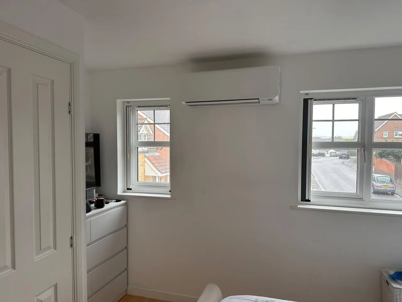 Wall-mounted air conditioning unit installed between two bedroom windows