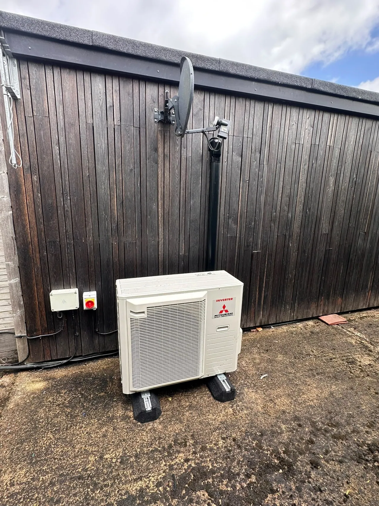 Mitsubishi air conditioning outdoor condenser installed on anti-vibration feet by a shed
