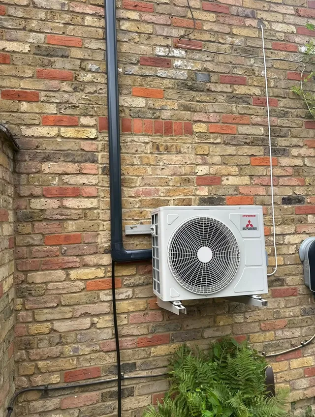 Mitsubishi air conditioning outdoor condenser installed wall-mounted above plants