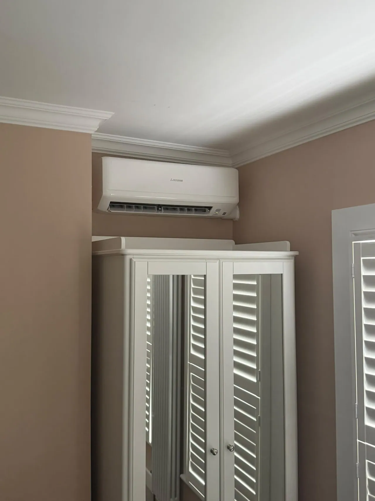 Wall-mounted air conditioning unit installed above a wardrobe