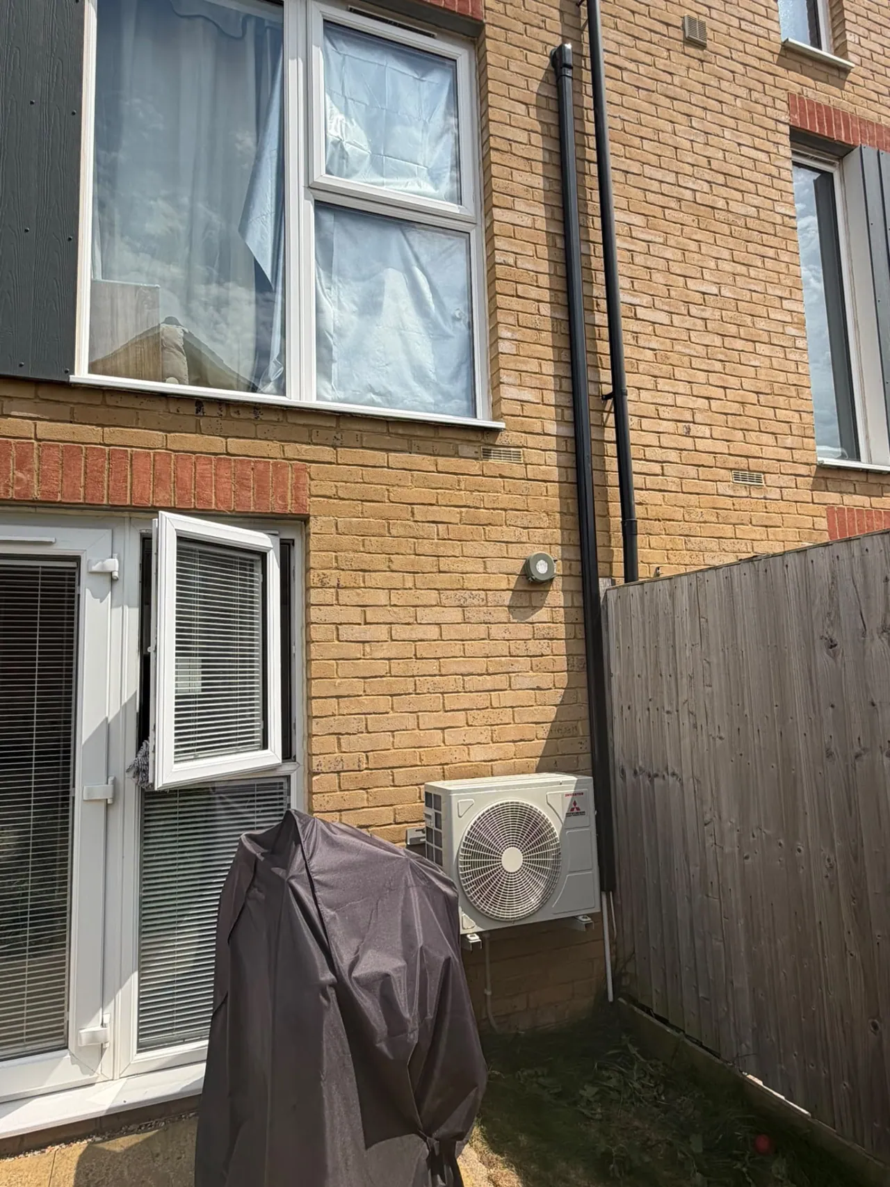 Mitsubishi air conditioning outdoor condenser installed beside a brick house and fence