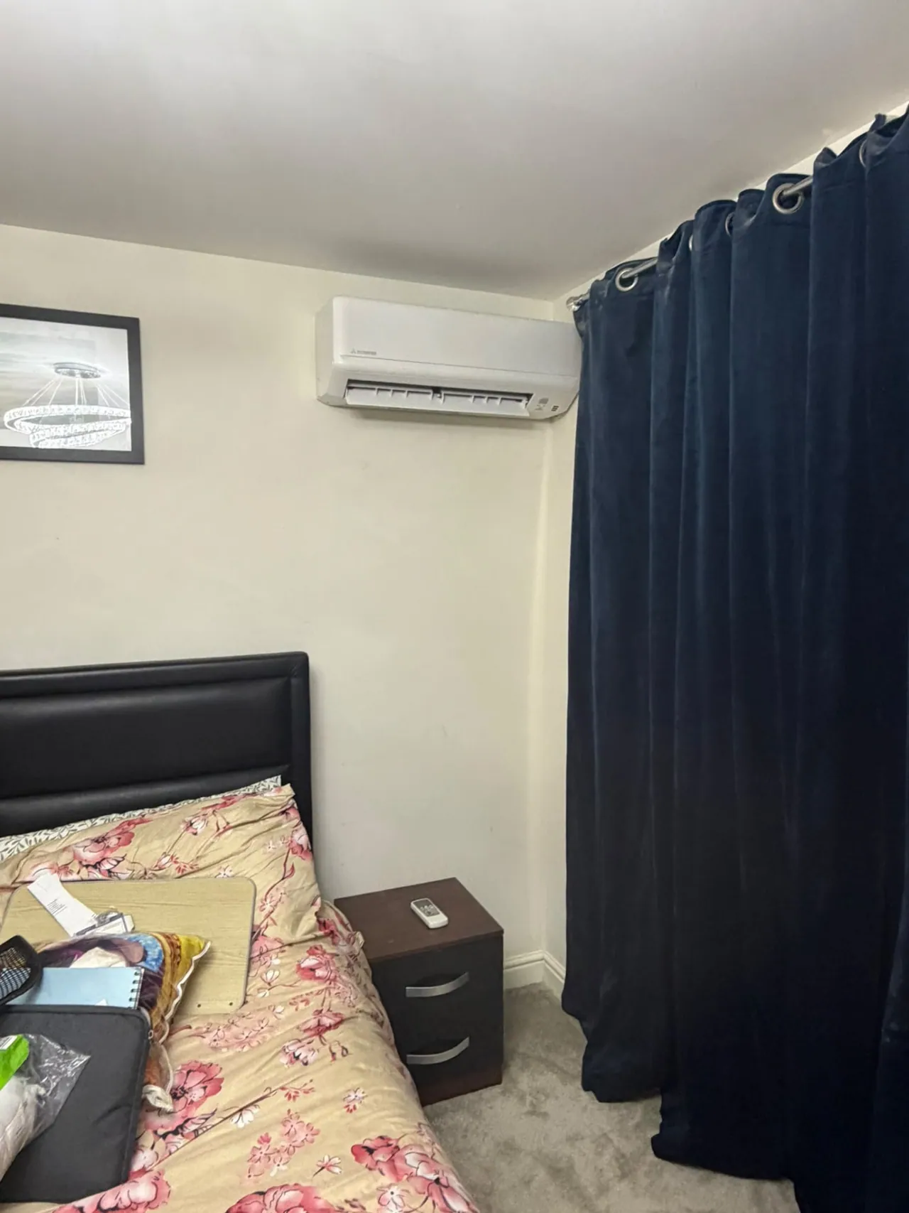 Wall-mounted air conditioning unit installed in a bedroom beside curtains
