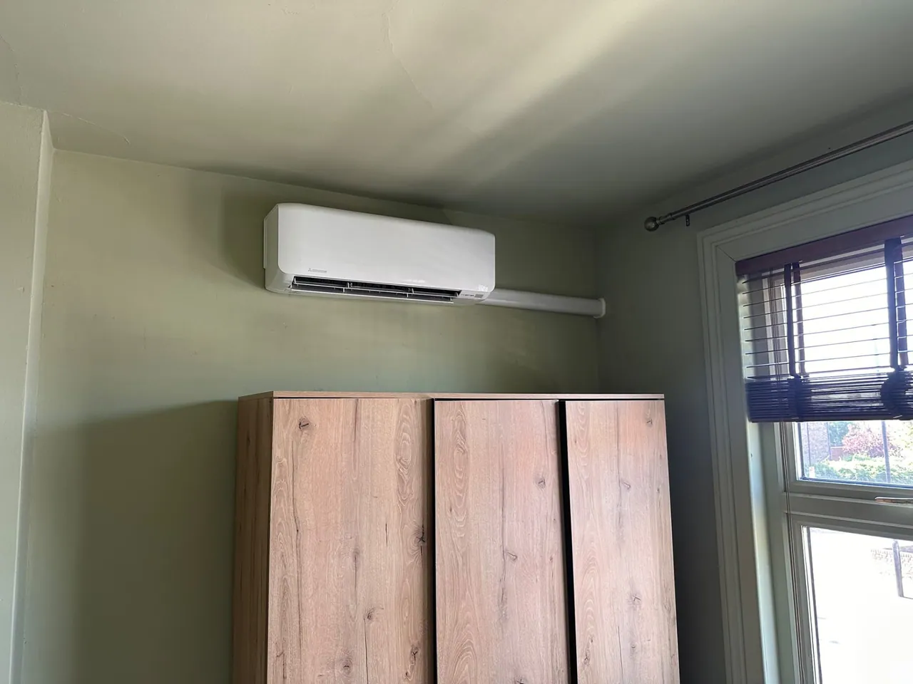 Wall-mounted air conditioning unit installed with neat white trunking above a cabinet