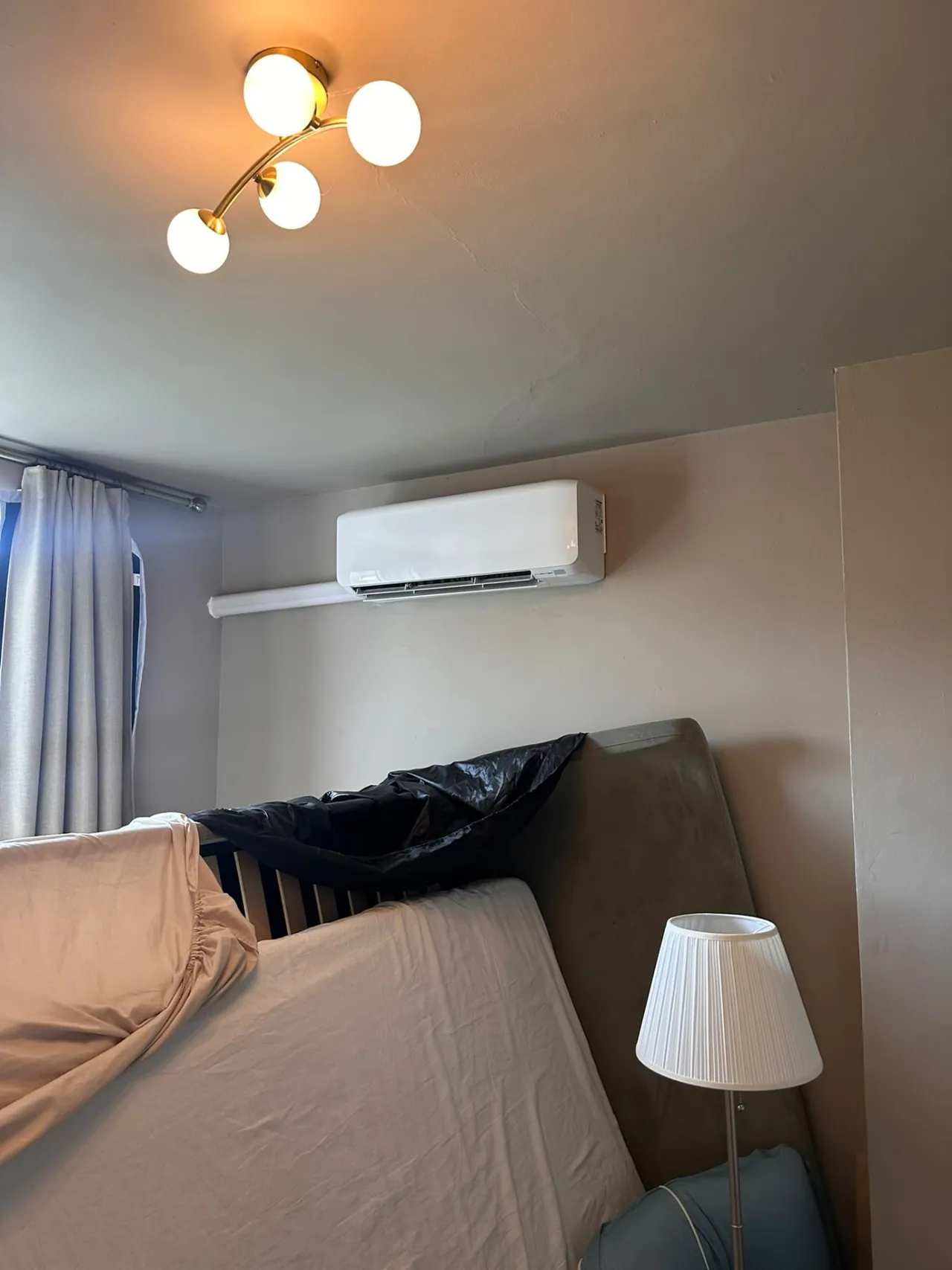 Wall-mounted air conditioning unit installed above a bed in a warm-toned bedroom